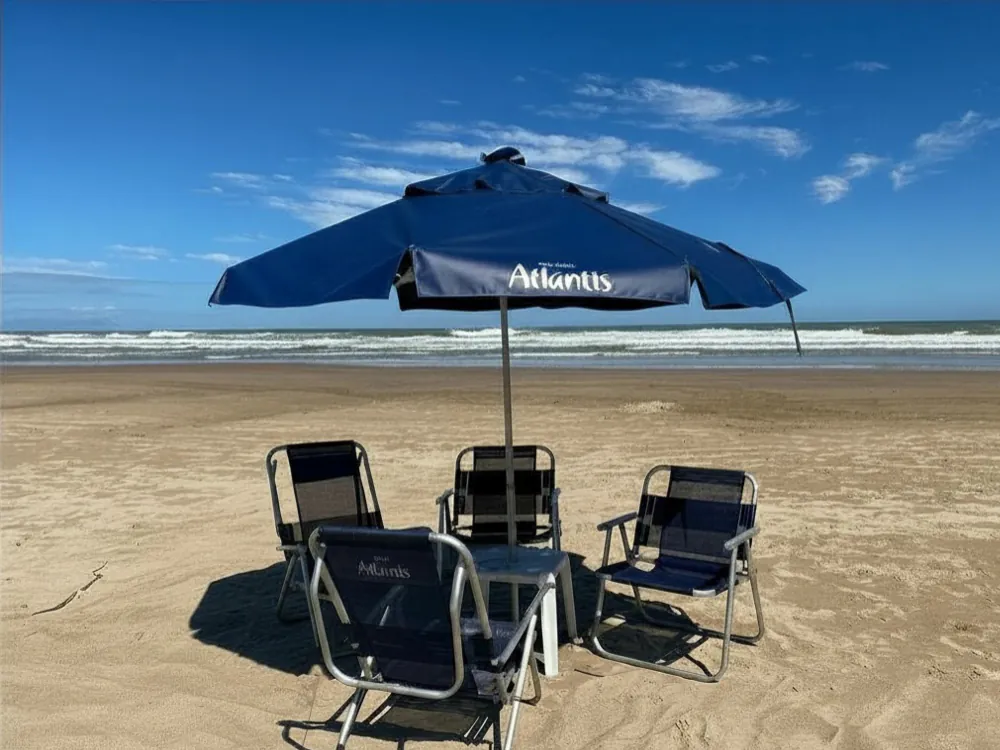 Guarda-sol e cadeiras do serviço de praia montados na areia, em frente ao prédio